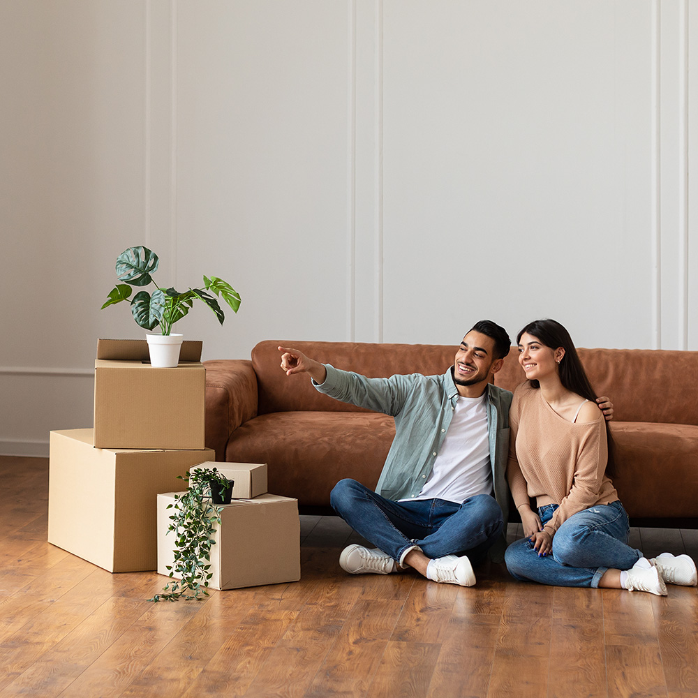 Portrait of smiling family sitting on the floor leaning on couch in new empty apartment.